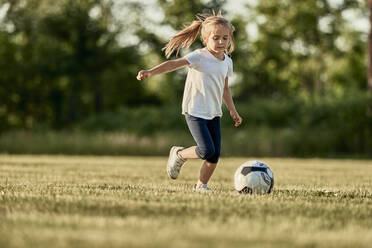 Blondes Mädchen spielt Fußball an einem sonnigen Tag - ZEDF04679