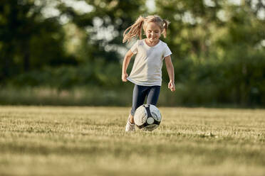 Glückliches blondes Mädchen spielt Fußball auf einem Sportplatz - ZEDF04680