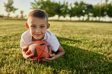Lächelnder Junge mit Rugbyball auf einem Sportplatz an einem sonnigen Tag - ZEDF04682