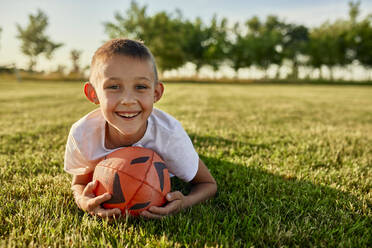 Glücklicher Junge mit Rugbyball auf einem Sportplatz an einem sonnigen Tag - ZEDF04684