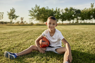 Lächelnder Junge mit Rugbyball auf einem Sportplatz an einem sonnigen Tag - ZEDF04687