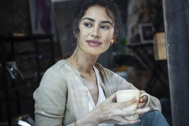 Lächelnde Frau mit Kaffeetasse schaut durch ein Fenster - JSRF02108