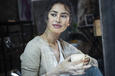 Smiling woman with coffee cup looking through window - JSRF02108