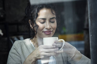 Schöne Frau mit geschlossenen Augen riecht Kaffee durch Glasfenster gesehen - JSRF02109