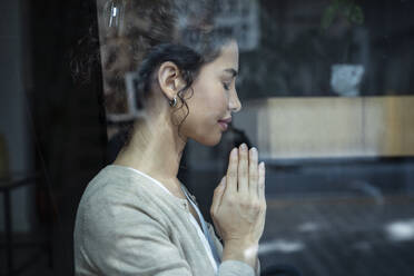 Woman with hands clasped seen through glass window - JSRF02110