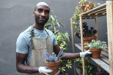 Lächelnder glatzköpfiger Mann mit Topfpflanzen im Garten stehend - JSRF02115
