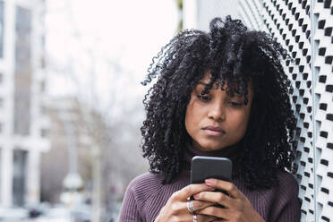 Serious woman using mobile phone by wall - PNAF04098