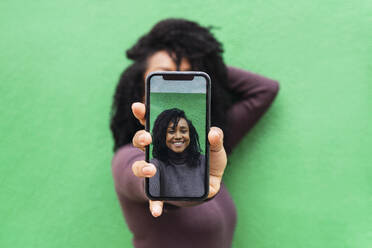 Hände einer Frau, die ein Selfie auf einem Smartphone vor einer grünen Wand macht - PNAF04108