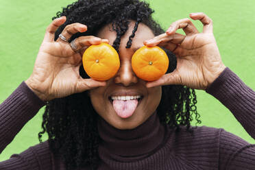 Woman sticking out tongue covering eyes with oranges - PNAF04111
