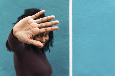 Woman gesturing stop sign in front of blue wall - PNAF04121