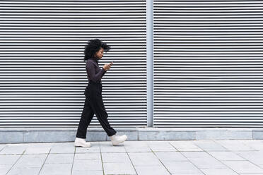 Frau, die ein Smartphone benutzt und an einer Wand vorbeiläuft - PNAF04136