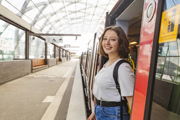 Smiling teenage girl standing at doorway of train at railroad station - IHF01025