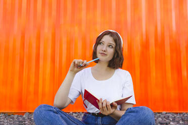 Nachdenkliches Teenager-Mädchen mit Notebook vor einem orangefarbenen Frachtcontainer - IHF01030