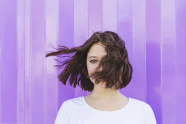 Teenage girl with tousled hair in front of purple cargo container - IHF01034