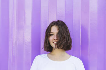 Smiling teenage girl with brown hair in front of purple cargo container - IHF01036