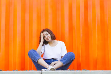 Smiling teenage girl sitting in front of orange cargo container - IHF01041