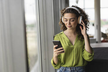 Geschäftsfrau trägt Kopfhörer und hört Musik über ihr Smartphone im Büro - JCICF00013