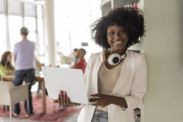 Smiling businesswoman with laptop leaning on rack at office - JCICF00024