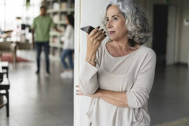 Businesswoman talking on speaker phone near column at office - JCICF00044