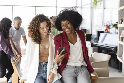 Glückliche Geschäftsfrauen teilen sich ein Smartphone im Büro - JCICF00064