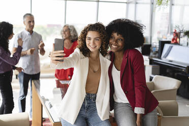 Lächelnde Geschäftskollegen machen ein Selfie mit ihrem Smartphone im Büro - JCICF00067