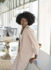 Businesswoman with curly hair leaning on table at office - JCICF00068