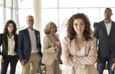 Confident businesswoman with arms crossed standing with colleagues in background at office - JCICF00093