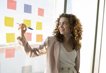 Smiling businesswoman explaining strategy over adhesive notes at office - JCICF00111