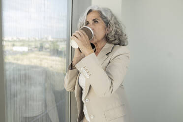 Geschäftsfrau trinkt im Büro Kaffee aus einem Einwegbecher - JCICF00114