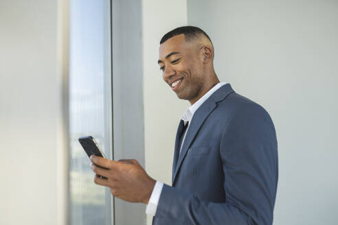 Lächelnder Geschäftsmann, der ein Smartphone im Büro benutzt - JCICF00117