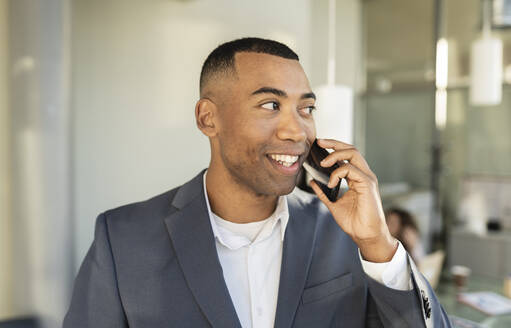 Nachdenklicher Geschäftsmann, der im Büro mit seinem Smartphone telefoniert - JCICF00118