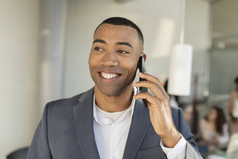 Glücklicher Geschäftsmann, der im Büro mit seinem Mobiltelefon spricht - JCICF00119