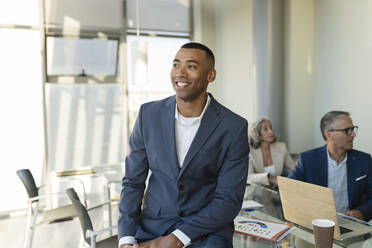 Smiling businessman sitting on table at office - JCICF00122