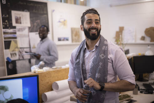 Smiling young businessman in scarf standing in office - CAIF32906