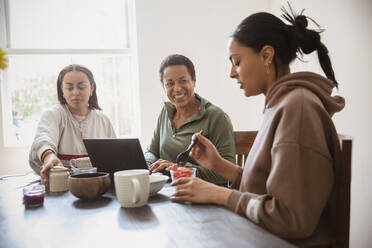 Happy mother and daughters eating breakfast at home - CAIF32921