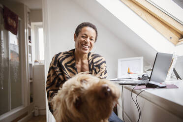 Porträt glückliche Frau mit Hund am Schreibtisch im Heimbüro - CAIF32949