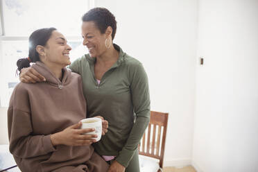 Happy mother and young adult daughter hugging at home - CAIF32951