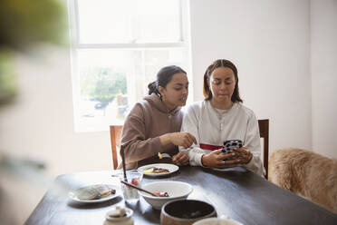 Junge erwachsene Schwestern benutzen ein Smartphone am Esstisch - CAIF32976