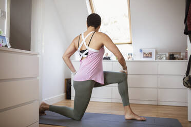 Woman exercising, practicing yoga twist on mat at home - CAIF32978