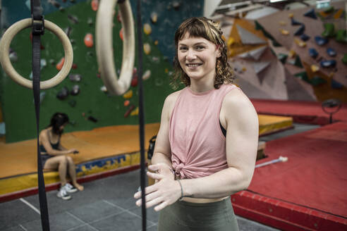 Portrait confident young woman chalking hands at climbing center - CAIF33034