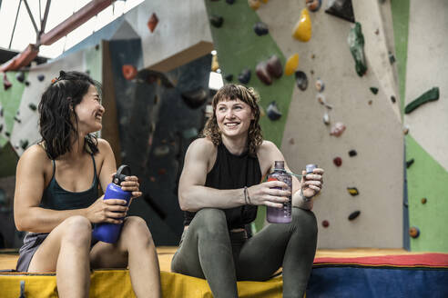Happy female rock climbers taking a break at climbing gym - CAIF33071