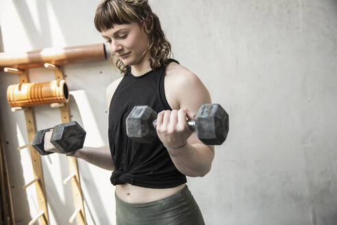 Junge Frau beim Gewichtheben mit Hanteln im Fitnessstudio - CAIF33076