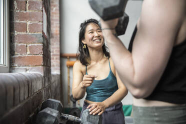 Glückliche Frau trainiert mit einem Freund im Fitnessstudio - CAIF33088