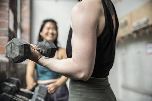 Nahaufnahme einer Frau, die mit einer Hantel im Fitnessstudio trainiert - CAIF33095