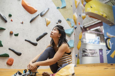 Weibliche Kletterin schaut auf die Kletterwand in der Turnhalle - CAIF33117