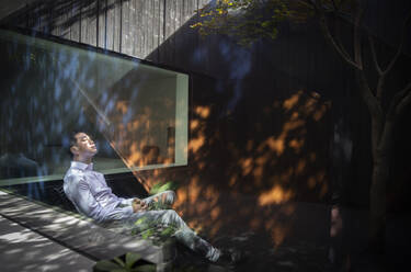 Gelassener Mann sitzt im Sonnenlicht im Innenhof - CAIF33183