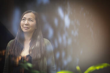 Smiling woman looking up at window with reflections - CAIF33200