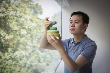 Man stacking wooden circles at window - CAIF33203