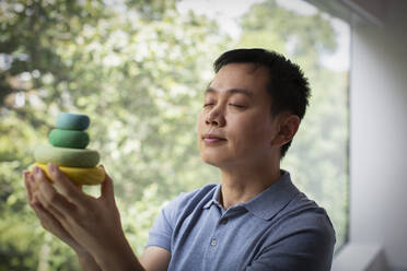 Serene man holding stacked wooden circles at window - CAIF33207