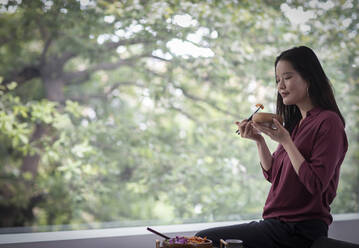 Junge Frau isst mit Stäbchen am Fenster - CAIF33208